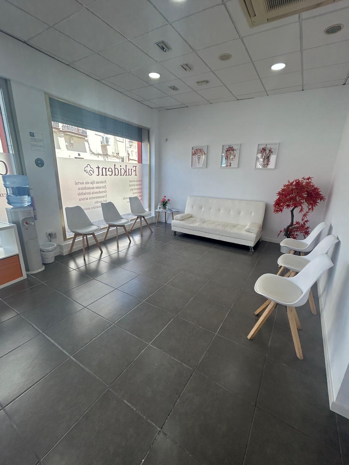 Sala de espera de Clínica Dental Fukident en Churriana, con sofá blanco y sillas junto al ventanal.
