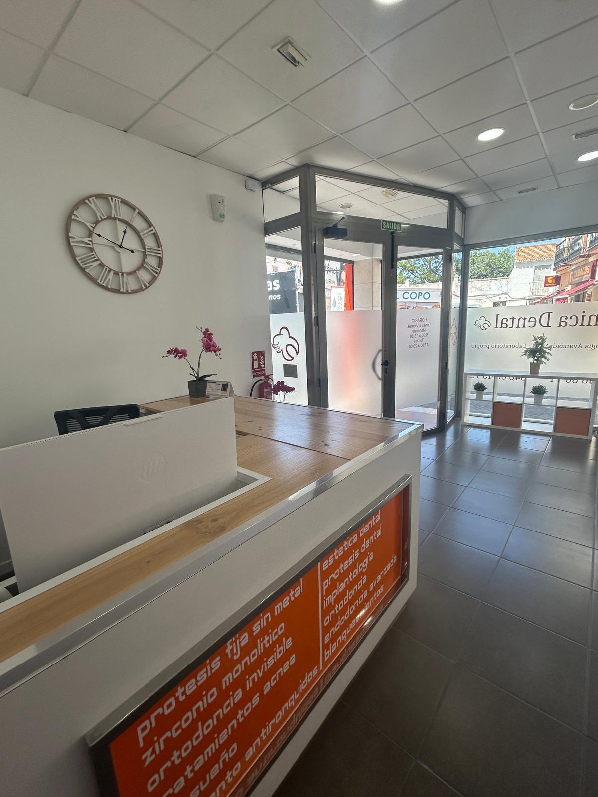 Recepción de Clínica Dental Fukident en Churriana, con mostrador blanco y madera junto a la entrada.